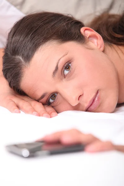 Крупним планом жінка в ліжку досягає свого мобільного телефону — стокове фото