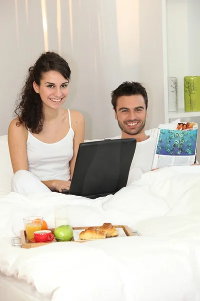 Пара в постели с ноутбуком и журналом — стоковое фото