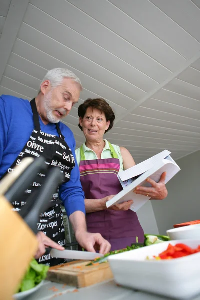 Mature couple cooking with cookbook — Stock Photo, Image