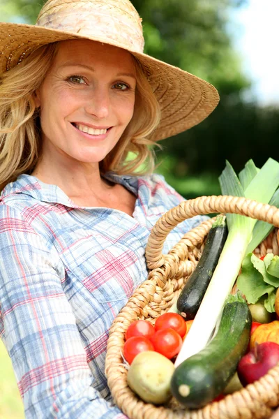 Femme avec un chapeau de paille tenant panier de légumes . — Photo