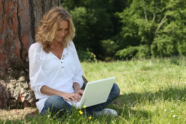 Женщина смеется над своим ноутбуком в парке — стоковое фото