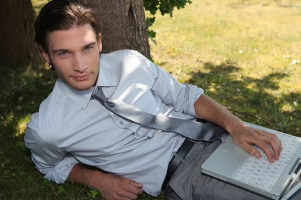 Młody człowiek siedzi na trawie z komputerem — Zdjęcie stockowe