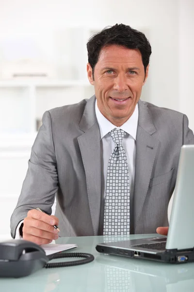 在他的桌前坐着一台便携式计算机的商人 — 图库照片