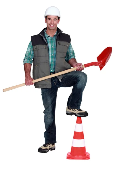 Tradesman holding a spade and propping his foot up on a pylon — Stock Photo, Image