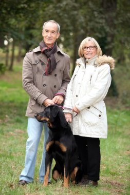 Mature couple walking in a park with their dog clipart