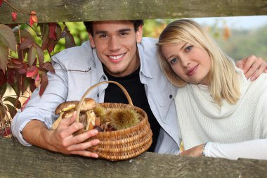 Young couple behind a wooden barrier in autumn, the man is holding a wicker clipart