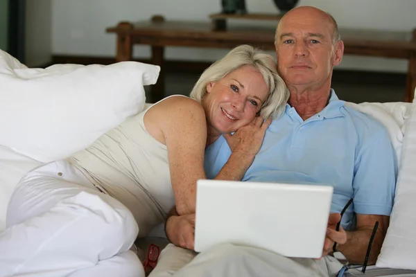 Coppia anziana seduta su un divano con un computer portatile — Foto Stock
