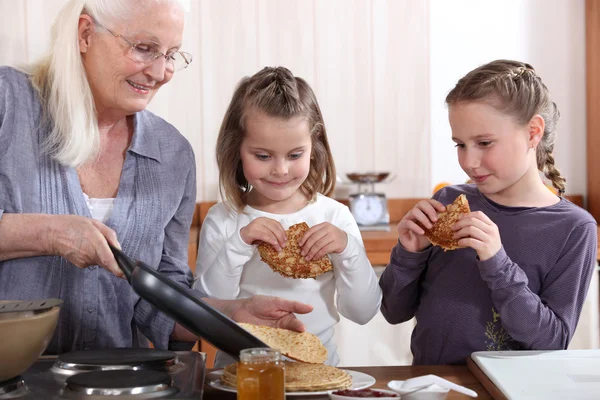 A grandmother cooking crepes for her granddaughters. — Stockfoto