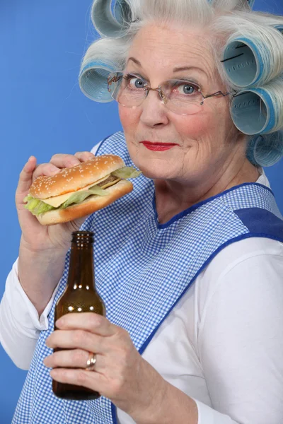 Vieille femme en rouleaux avec un hamburger et une bière — Photo
