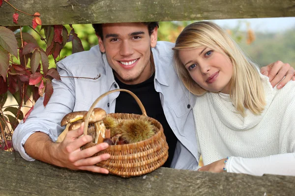 Młoda para za barierę drewnianą jesienią, człowiek trzyma wiklinowe — Zdjęcie stockowe
