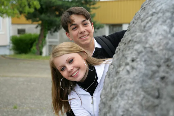 Adolescents peering out from behind a rock — Stock Photo, Image