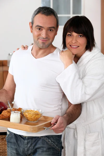 Un uomo che porta la colazione su un vassoio e sua moglie che indossa un accappatoio — Foto Stock