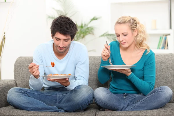 Casal comendo jantar em um sofá — Fotografia de Stock