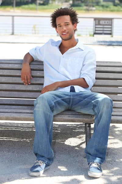 Mladý muž sedící na lavičce u řeky — Stock fotografie