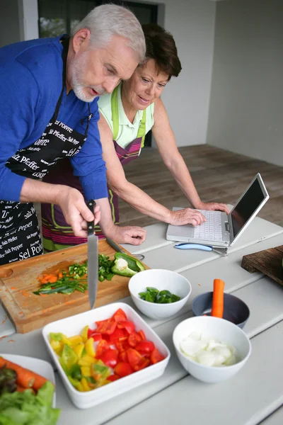Ζευγάρι προετοιμασία λαχανικών και κοιτάζοντας ένα φορητό υπολογιστή — Φωτογραφία Αρχείου