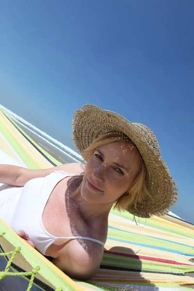 Mulher usando um chapéu de palha lounging em uma rede perto da praia — Fotografia de Stock