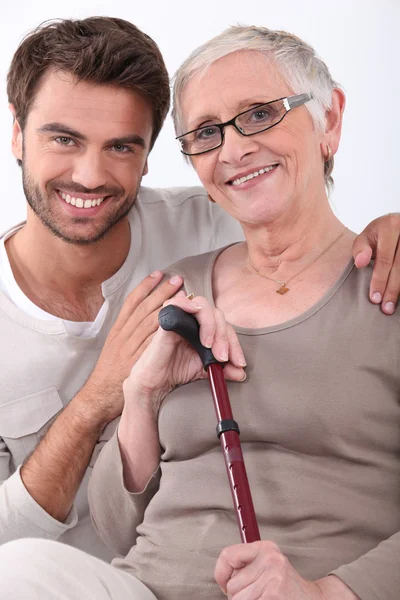 Jovem sorridente com os braços ao redor de uma mulher idosa de óculos — Fotografia de Stock