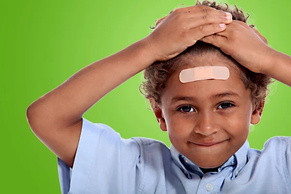Coloured little boy with plaster on his forehead against fluorescent green — Stock Photo, Image