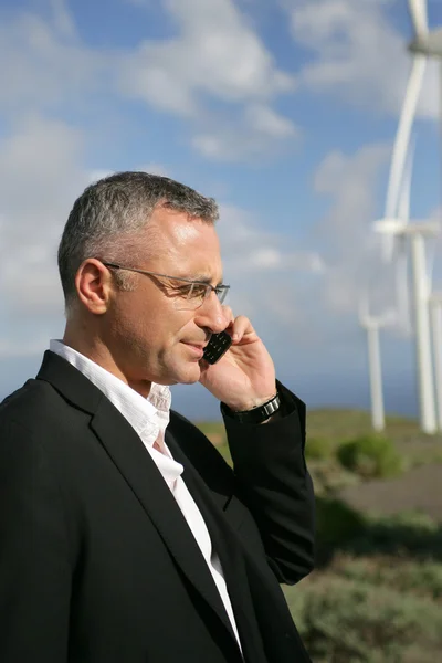 Empresário falando em seu telefone celular em um parque de turbinas eólicas — Fotografia de Stock