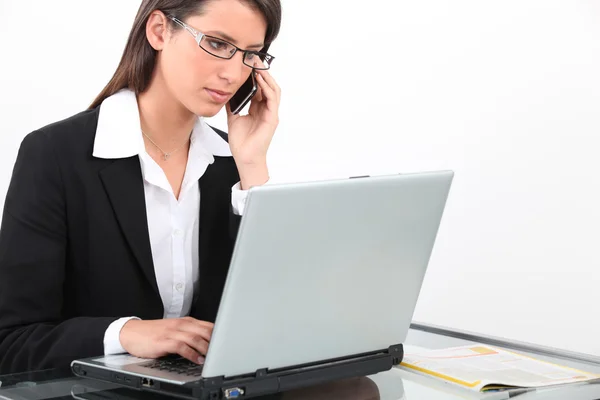 Brunette zakenvrouw met behulp van laptop en mobiele telefoon — Stockfoto
