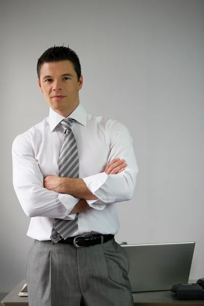Serious businessman man by his desk arms folded — Stock Photo, Image