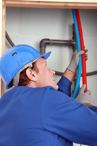 Plumber feeding hot and cold pipes behind a wall — Stock Photo, Image