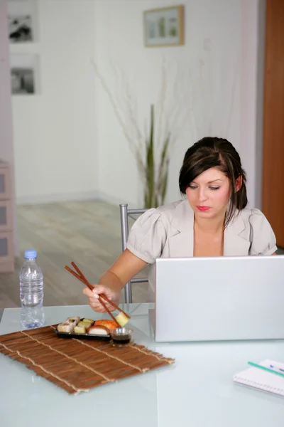 Женщина ест суши во время использования ноутбука — стоковое фото