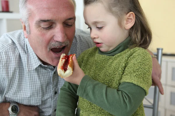 Kleindochter geven haar grootvader een stuk brood met jam te eten — Stockfoto
