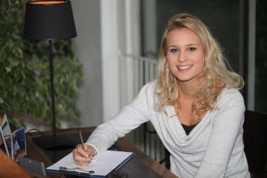 Young blond woman writing on clipboard clipart