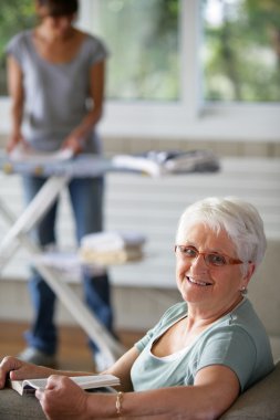 Portrait of a senior woman smiling on a sofa in front of a young woman fold clipart