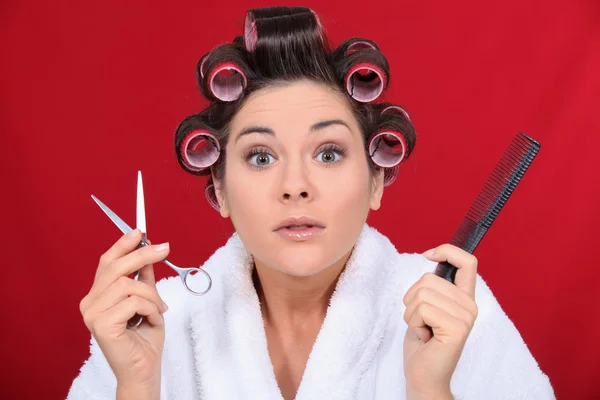Žena s vlasy na natáčky drží nůžky a hřeben — Stock fotografie