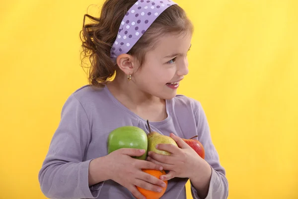 Ein kleines Mädchen mit ihren Armen voller Früchte. — Stockfoto