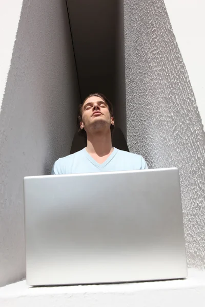 Man i en alkov basking i solskenet samtidigt som använder en bärbar dator — Stockfoto