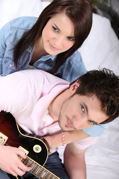Ett ungt par på säng, mannen spelar gitarr — Stockfoto