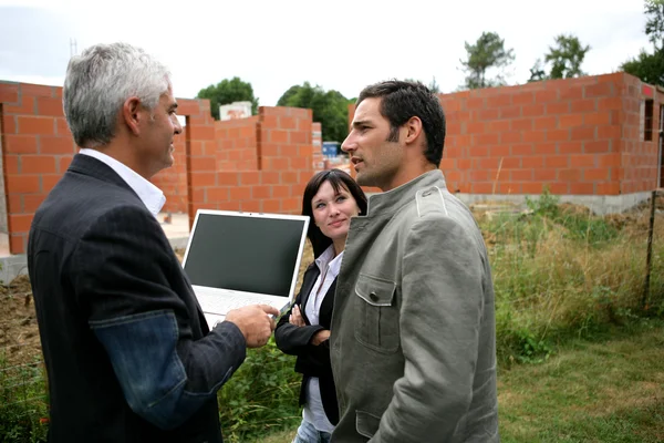 Couple and agent looking at a new-build holding a laptop with the screen le — Stock Photo, Image