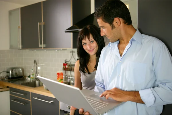 Пара стояла на кухне с ноутбуком — стоковое фото