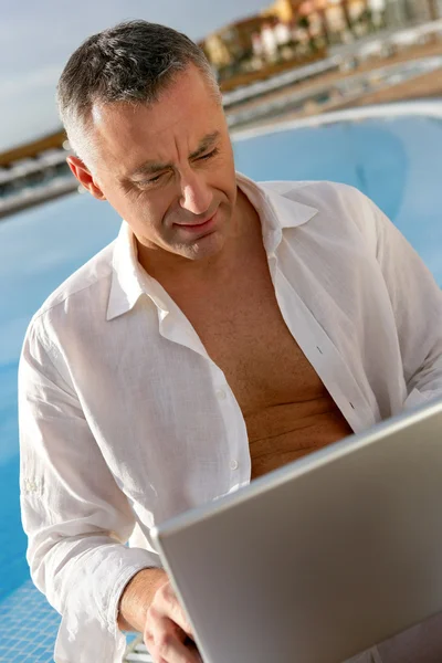 Чоловік сидить біля басейну перед портативним комп'ютером — стокове фото