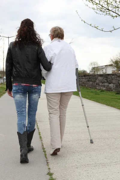 Mujer joven ayudando a anciana a caminar —  Fotos de Stock