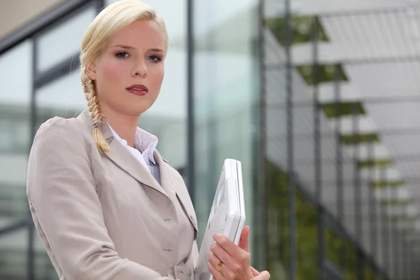 Femme d'affaires blonde tenant ordinateur portable à l'extérieur du bâtiment en verre — Photo