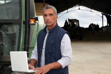 Farmer with laptop stood by tractor clipart