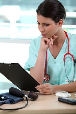 Female nurse reading medical record clipart