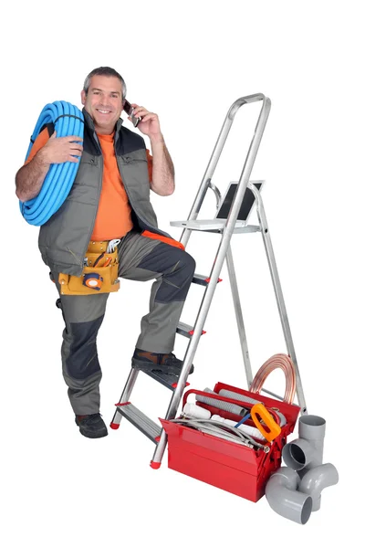 Plumber on the phone next to stepladder with laptop — Stock Photo, Image