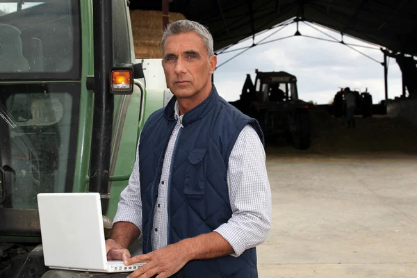 Фермер с ноутбуком стоял рядом с трактором — стоковое фото