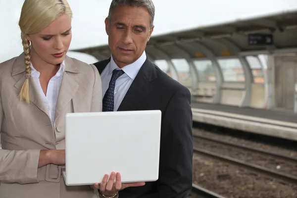 Casal de negócios com um laptop em uma plataforma ferroviária — Fotografia de Stock