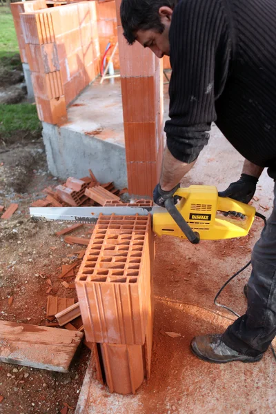 Man using a chainsaw to cut through a brick — Stock Photo, Image