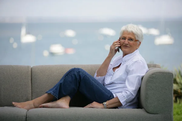 Starší žena seděla volání na venkovní sofa — Stock fotografie