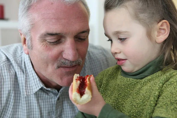 Mädchen füttert ihren Großvater mit Brot und Marmelade — Stockfoto