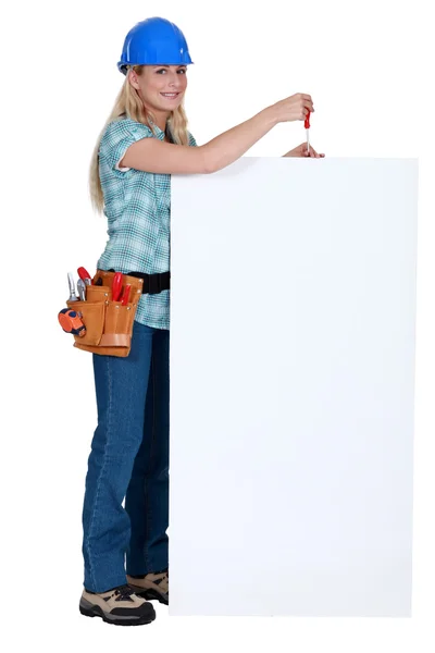Tradeswoman segurando uma chave de fenda sobre um sinal em branco — Fotografia de Stock