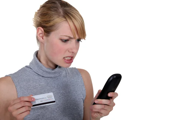 Mulher nervosa com cartão de crédito e telefone — Fotografia de Stock