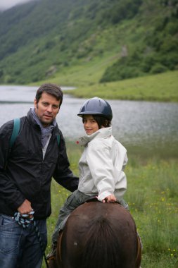 Man teaching his child how to ride a horse clipart